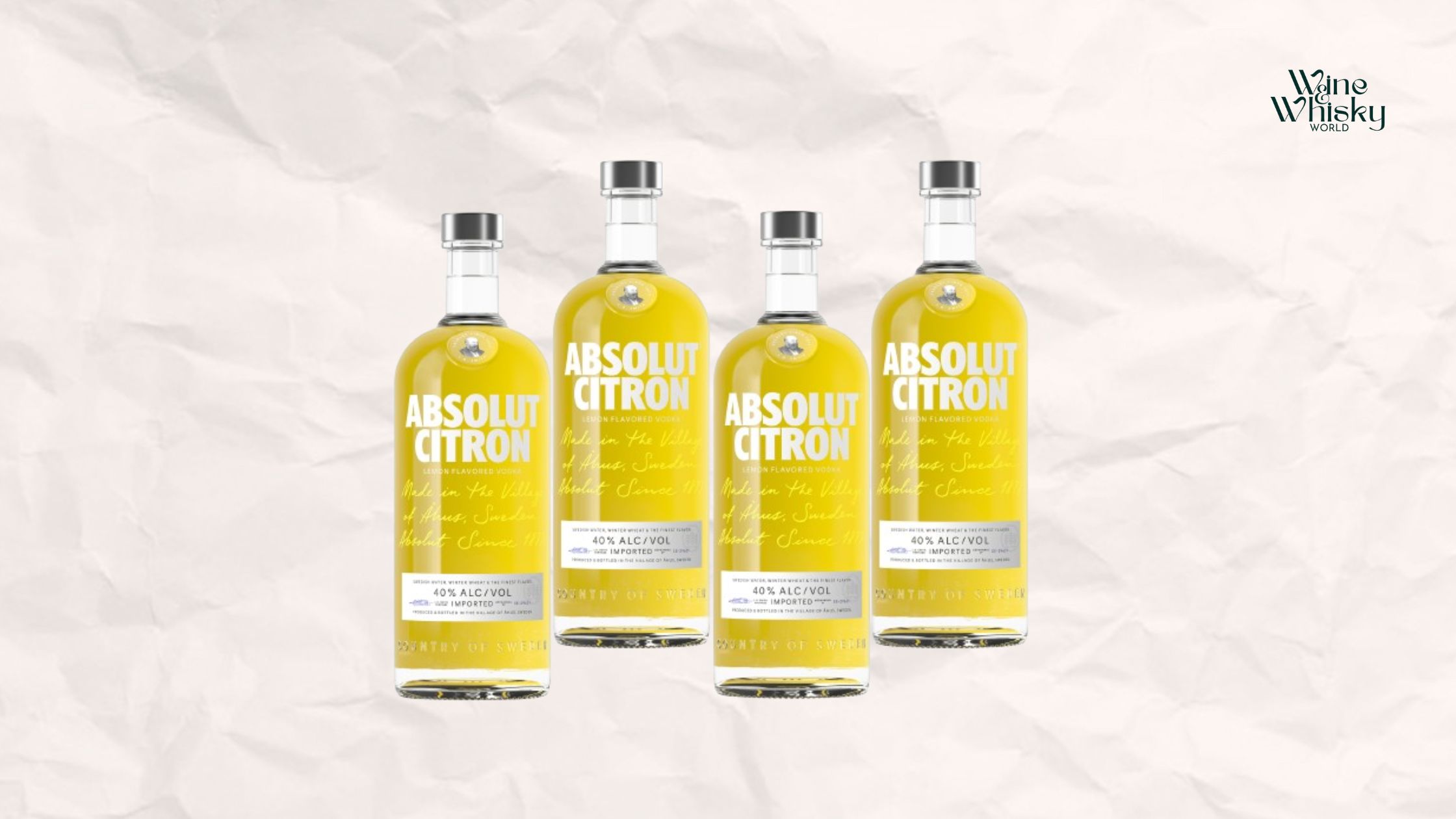 Clear glass bottle of Absolut Vodka with yellow and black text on the label, reading 'Absolut ', displayed against a crumpled white paper background with the Wine Whisky World logo in the top right corner.